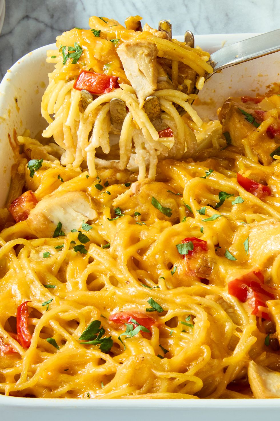 chicken, spaghetti, and red peppers covered in cheese in a casserole