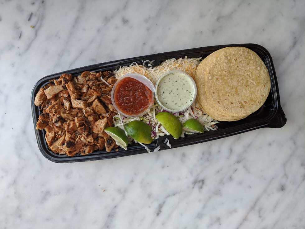 costco chicken street tacos in package including piles of seasoned chunks of chicken, red salsa and cilantro cream, shredded lettuce and cheese and corn tortillas