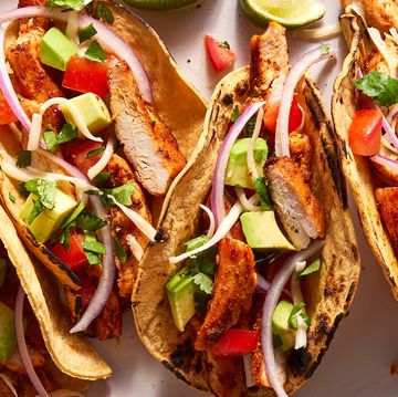 flour tortillas on a plate filled with chicken, tomatoes, avocado and red onion