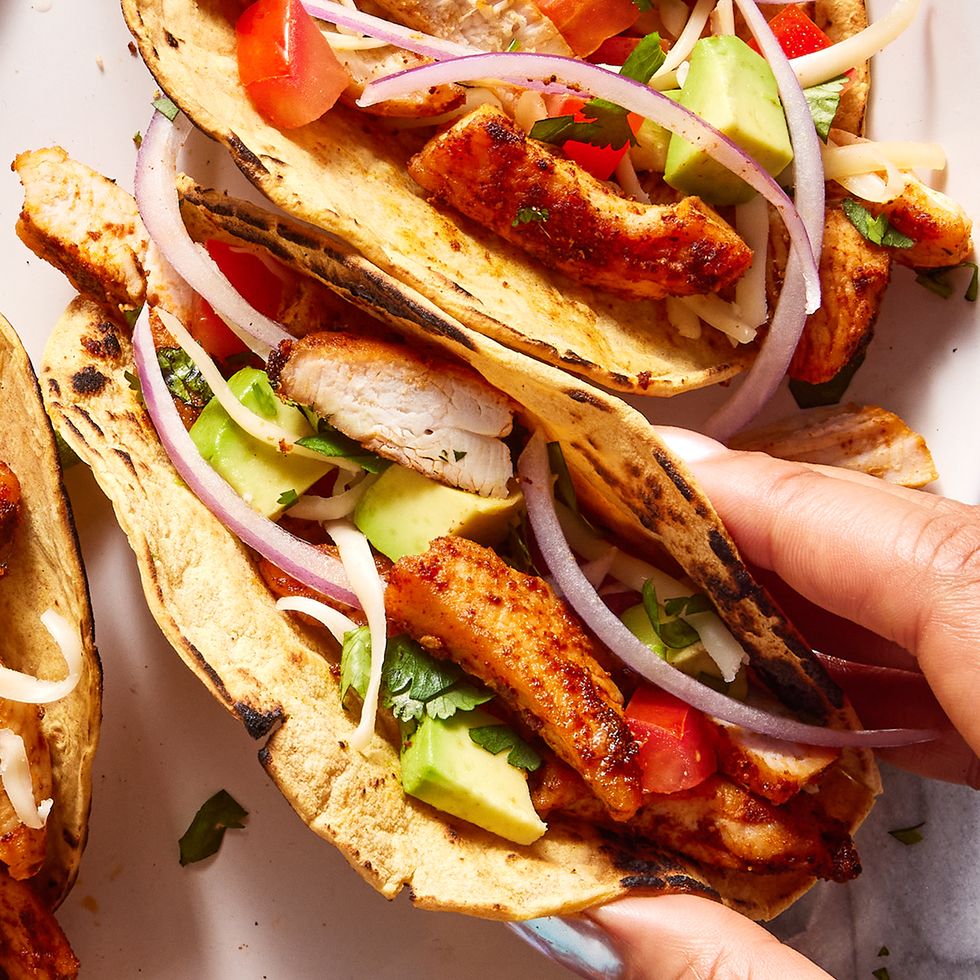flour tortillas on a plate filled with chicken, tomatoes, avocado and red onion