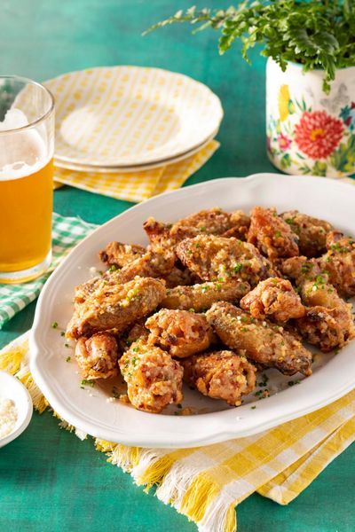 garlic parmesan chicken wings on white platter with glass of beer on green background