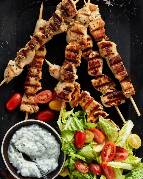chicken souvlaki skewers with a bowl of tzatziki, chopped romaine, and baby tomatoes on a black platter chicken souvlaki skewers with a bowl of tzatziki, chopped romaine, and baby tomatoes on a black platter