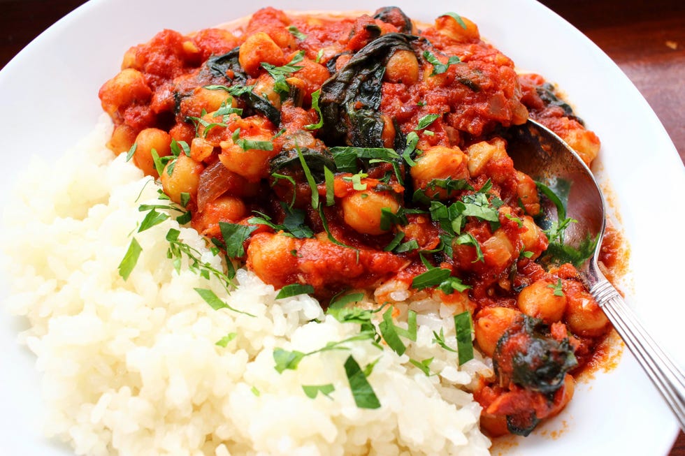 red tomato chickpea stew with spinach and white rice on a white plate, against a wooden background