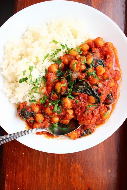 red tomato chickpea stew with spinach and white rice on a white plate, against a wooden background