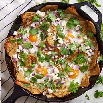 chilaquiles verde garnished with red onion, cilantro, and crumbled cheese in a black cast iron pan