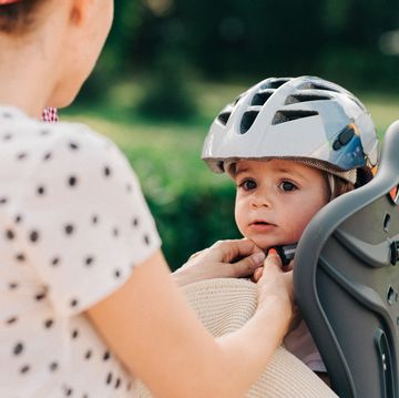 parent strapping toddler wearing helmet into child bike seat