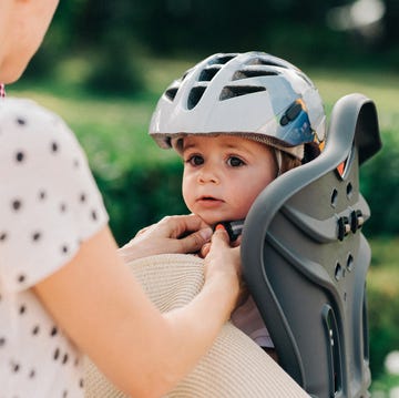 parent strapping toddler wearing helmet into child bike seat