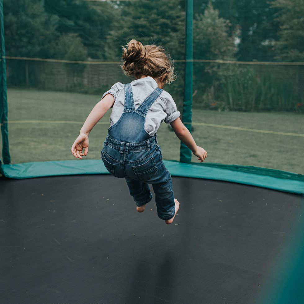 a child bounces on a large trampoline outside