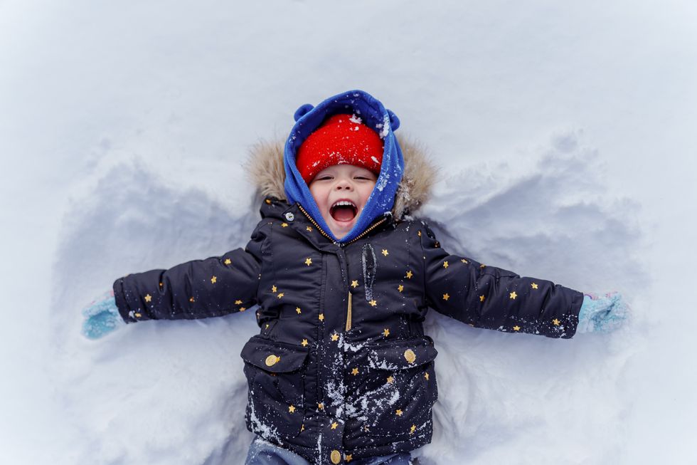 young child in snow making snow angel
