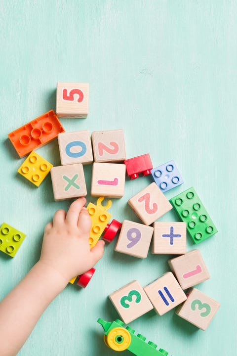 Child playing with wooden cubes with numbers and colorful toy bricks on a turquoise wooden background. Toddler learning numbers. Hand of a child taking toys.