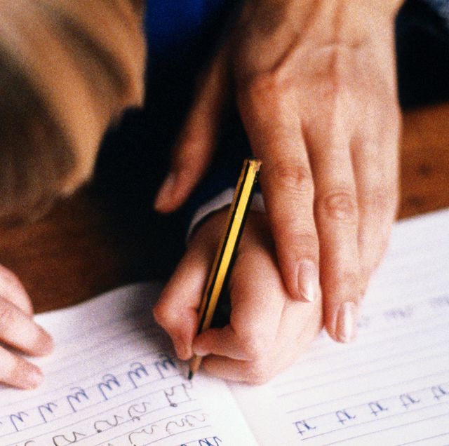 left handed child practicing writing in book guided by adult closeup