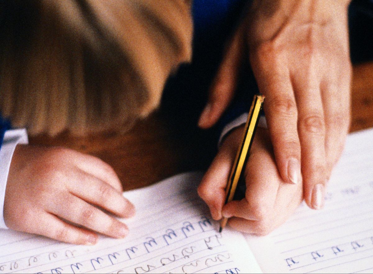 left handed child practicing writing in book guided by adult closeup