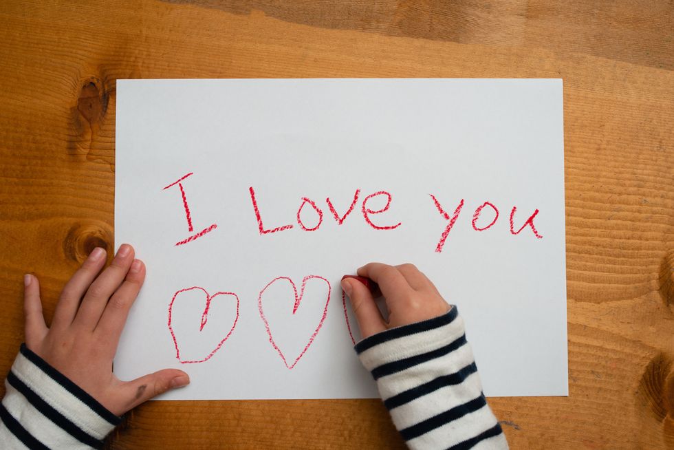 child writes i love you on paper