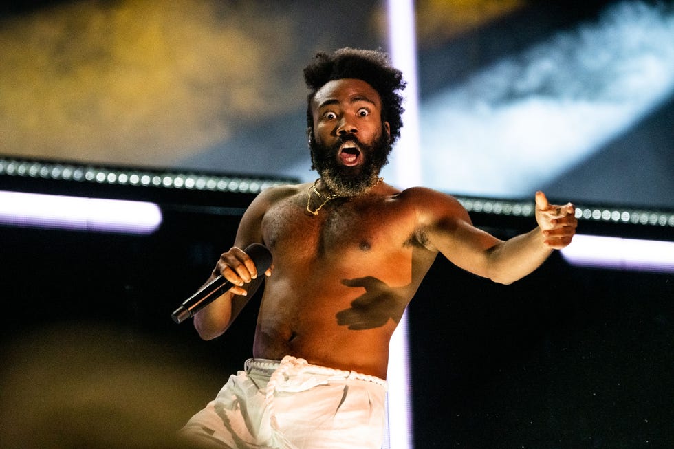 childish gambino holding a microphone and pointing out while performing shirtless