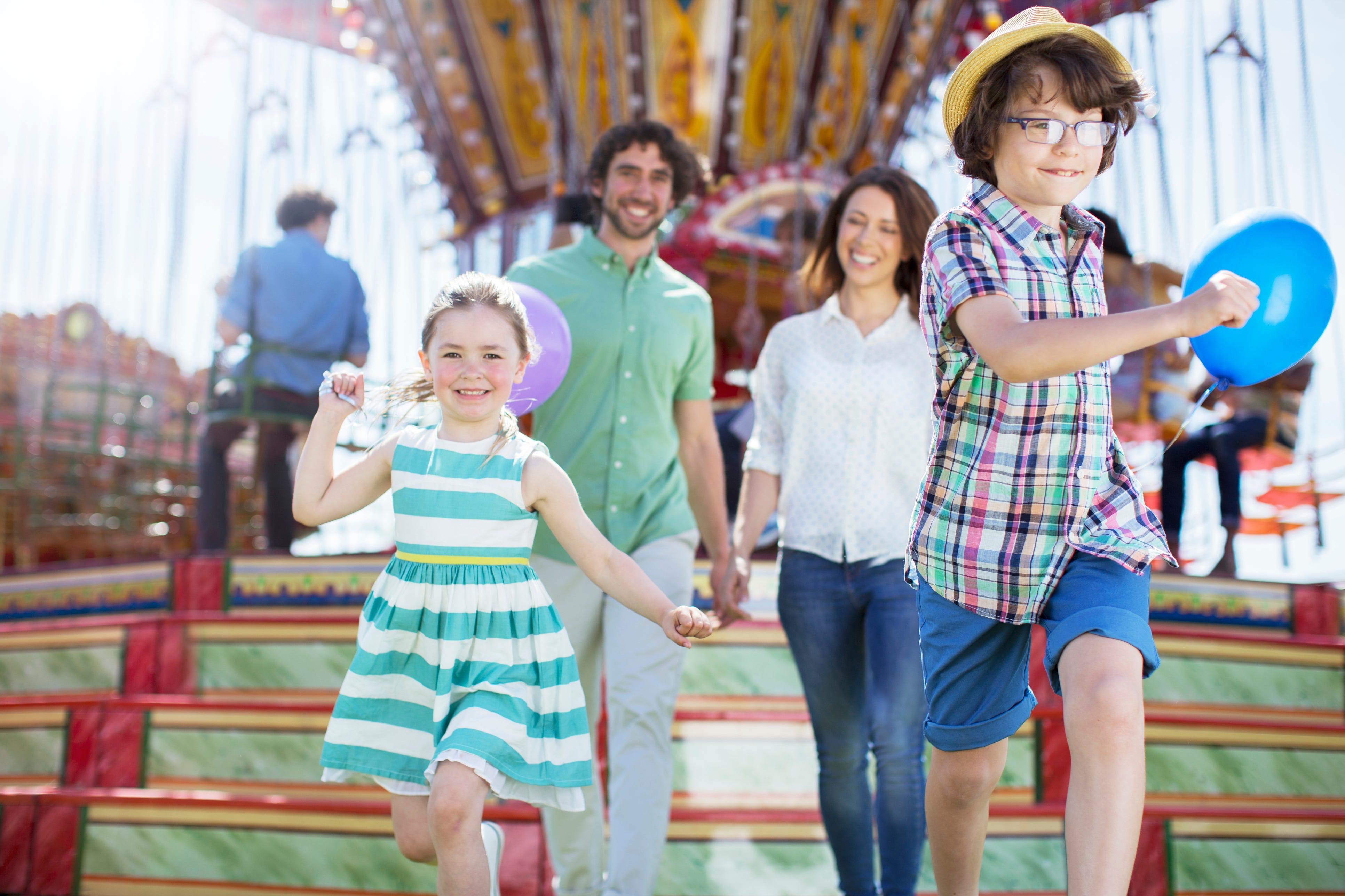 Children running in front of carousel, parents following them