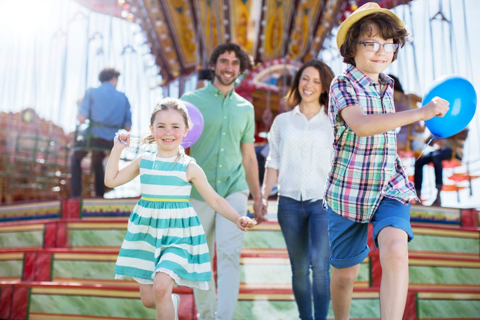 Children running in front of carousel, parents following them