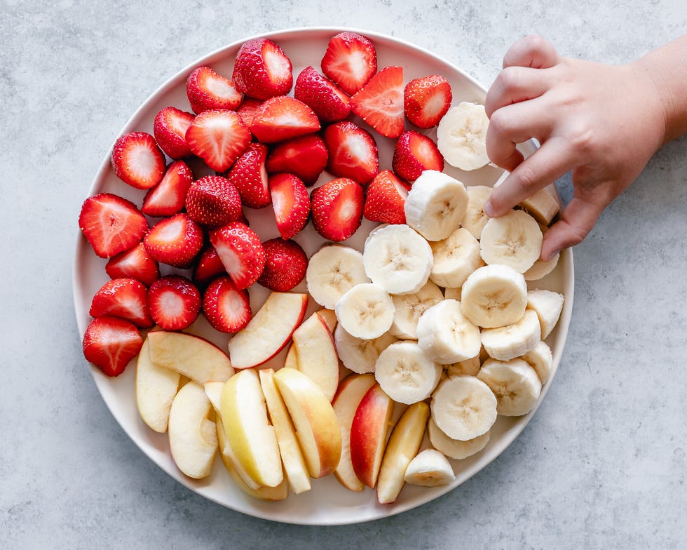 child's hand reaching for banana on a fruit snack platter