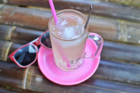 chilled coconut water in a glass with a pink straw on a pink plate next to pink sunglasses