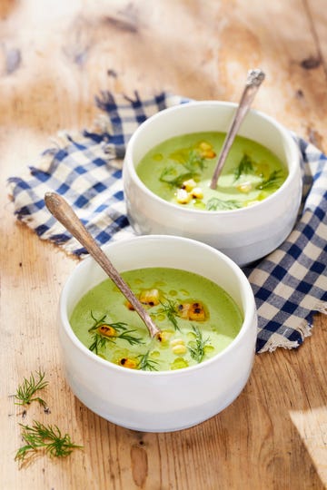 two bowls of chilled corn and dill soup with dill garnish on a wooden table