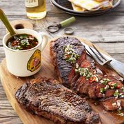 two steaks on a cutting board with chimichurri sauce spread on one