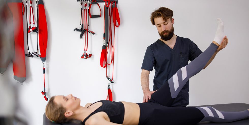 chiropractor stretches a female patient leg male physiotherapist is helping woman stretching his leg in exercise room