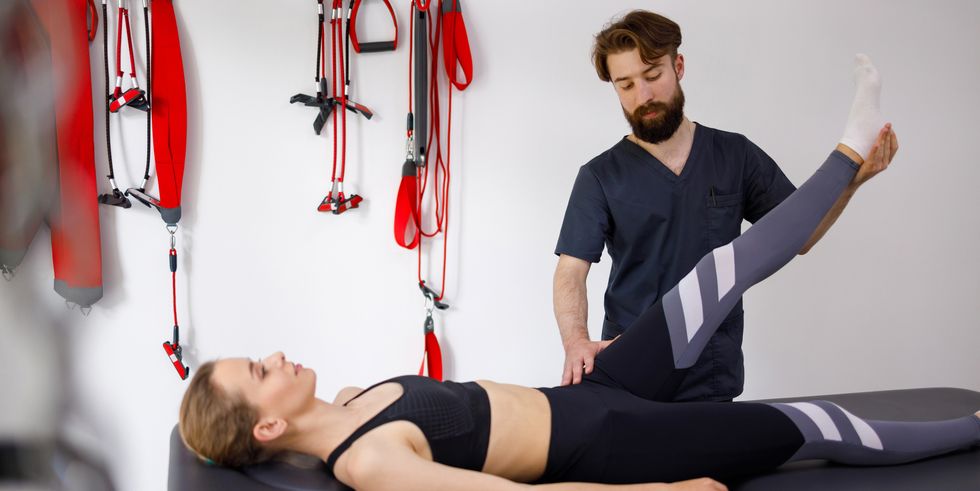 chiropractor stretches a female patient leg male physiotherapist is helping woman stretching his leg in exercise room
