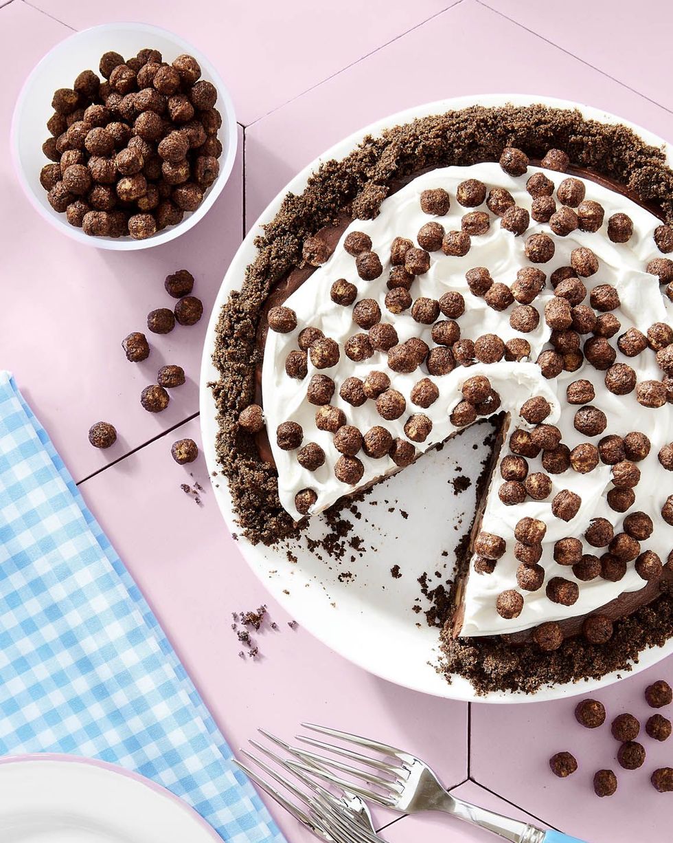 cocoa puffs and banana chocolate pie with whipped cream and cocoa puffs on top in a white pie dish with a slice removed