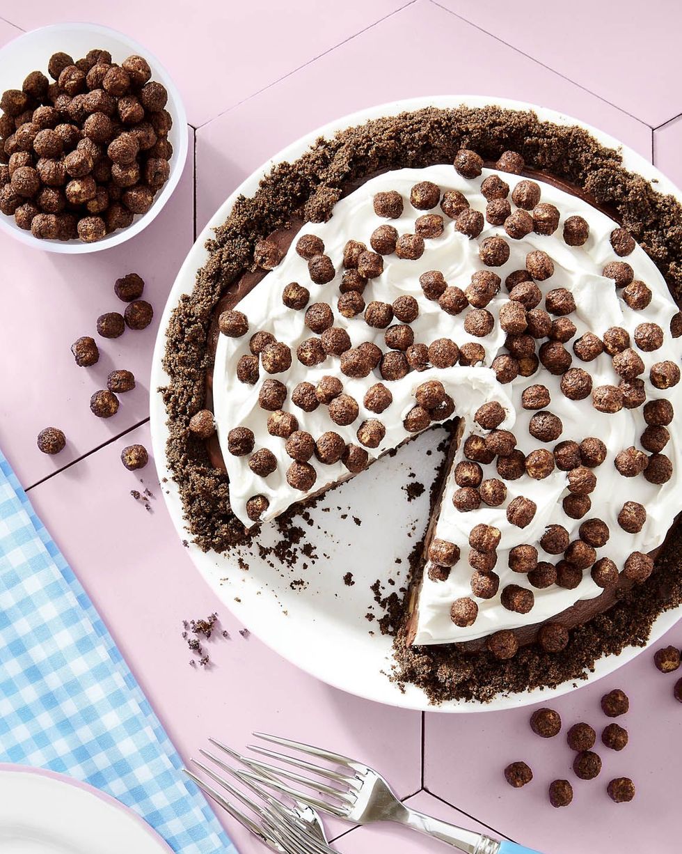 cocoa puffs and banana chocolate pie with whipped cream and cocoa puffs on top in a white pie dish with a slice removed