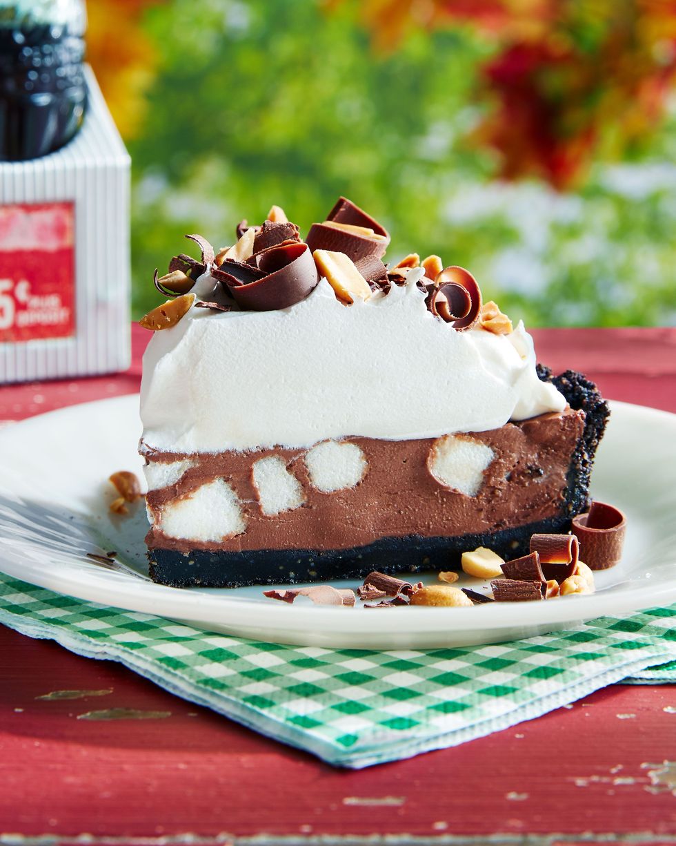 a slice of rocky road pie on a white plate with whipped cream chocolate curled and chopped peanuts on top
