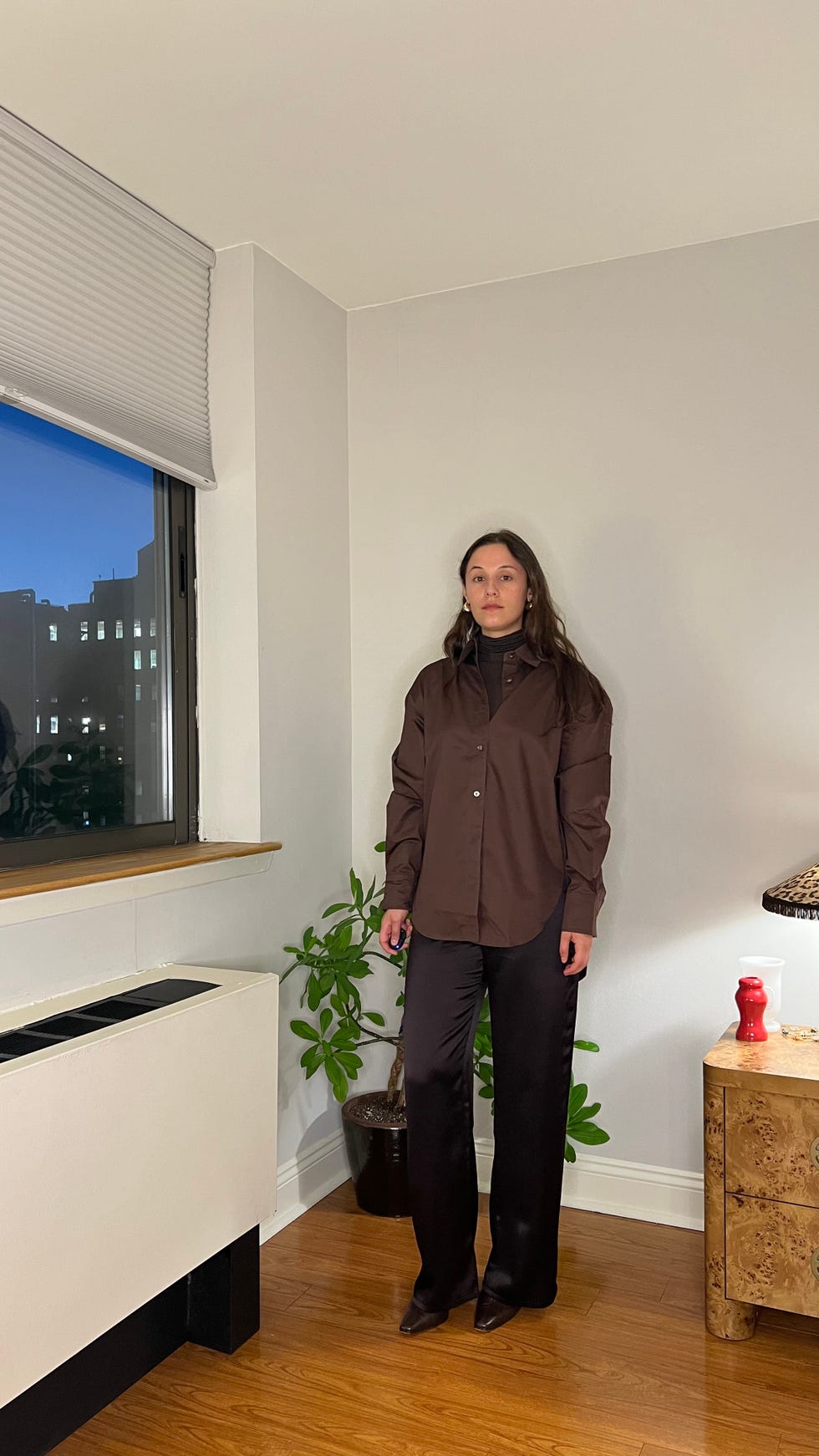 individual standing in a welllit room wearing dark clothing with plants and furniture in the background