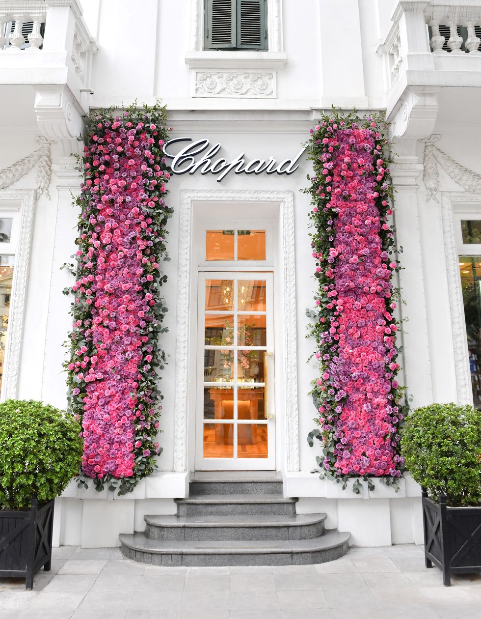 a white house with a large door and a large tree with pink flowers