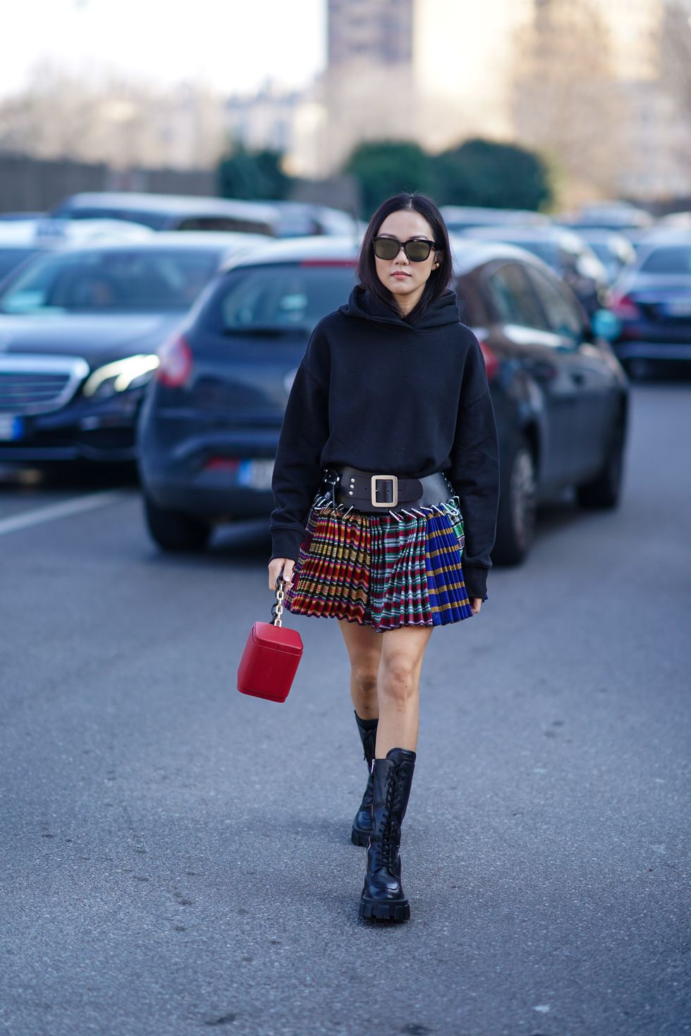 milan, italy february 22 yoyo cao wears sunglasses, a black hooded sweatshirt, a black belt, a colorful pleated mini skirt, a red bag, black prada mid calf lace up platform boots, outside msgm, during milan fashion week fallwinter 2020 2021 on february 22, 2020 in milan, italy photo by edward berthelotgetty images