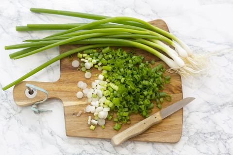 chopped and whole spring onions on wooden board