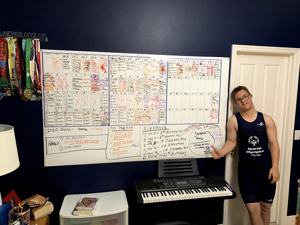 chris nikic stands next to his whiteboard that tracks all of his workouts and his dreams