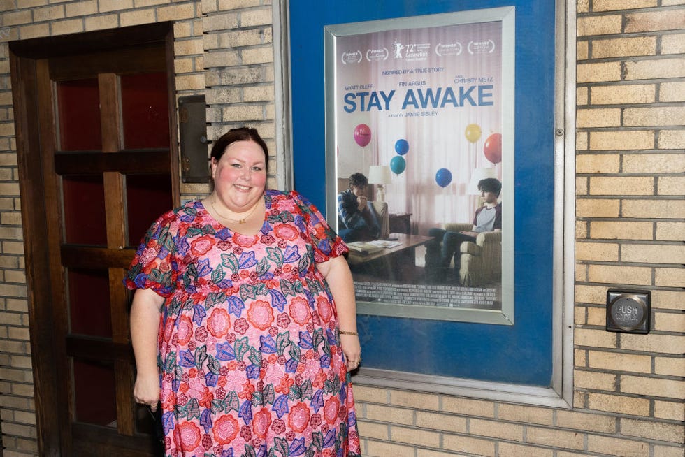 chrissy metz poses next to a stay awake poster