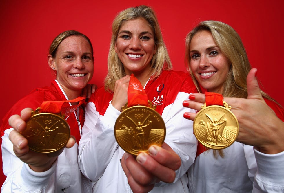 christie rampone, hope solo, and heather mitts smile and hold olympic medals around their neck toward the camera