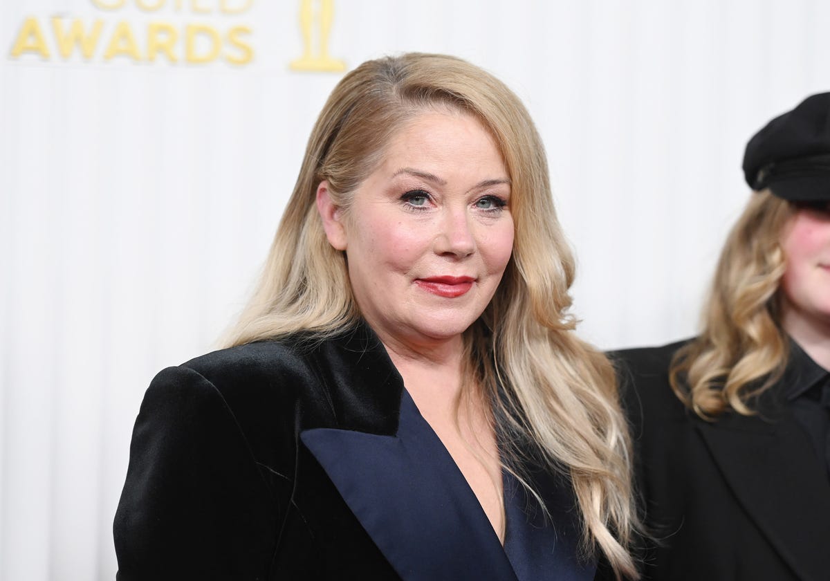 christina applegate, wearing a dark blue dress, looks off camera while standing next to another person who is partially visible in the photo