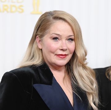 christina applegate smiles at the camera, she wears a velvet blazer and stands in front of a white background