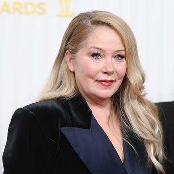 christina applegate smiles at the camera, she wears a velvet blazer and stands in front of a white background