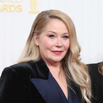 christina applegate smiles at the camera, she wears a velvet blazer and stands in front of a white background