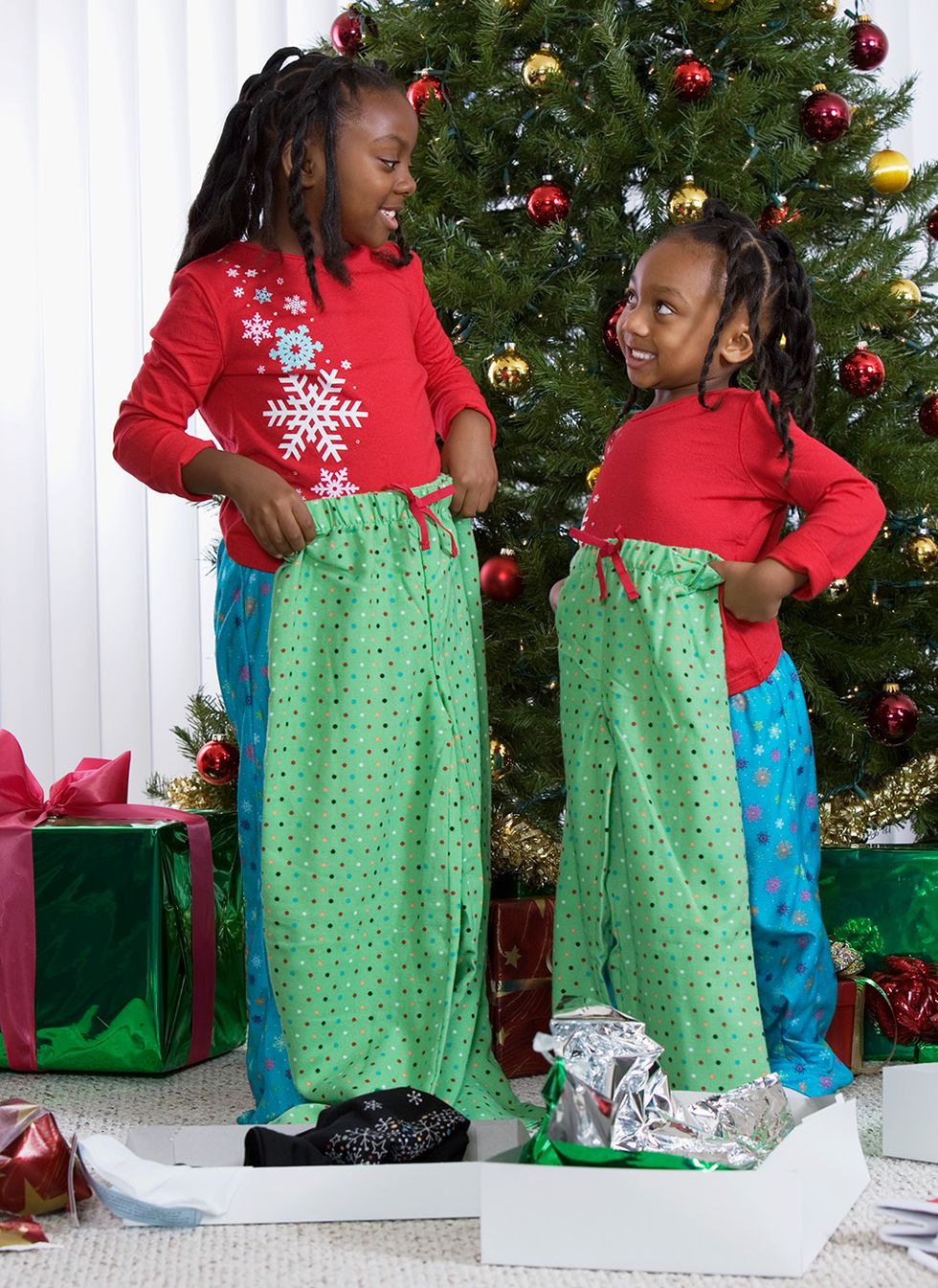 two young sisters holding matching pajama pants in front of a christmas tree