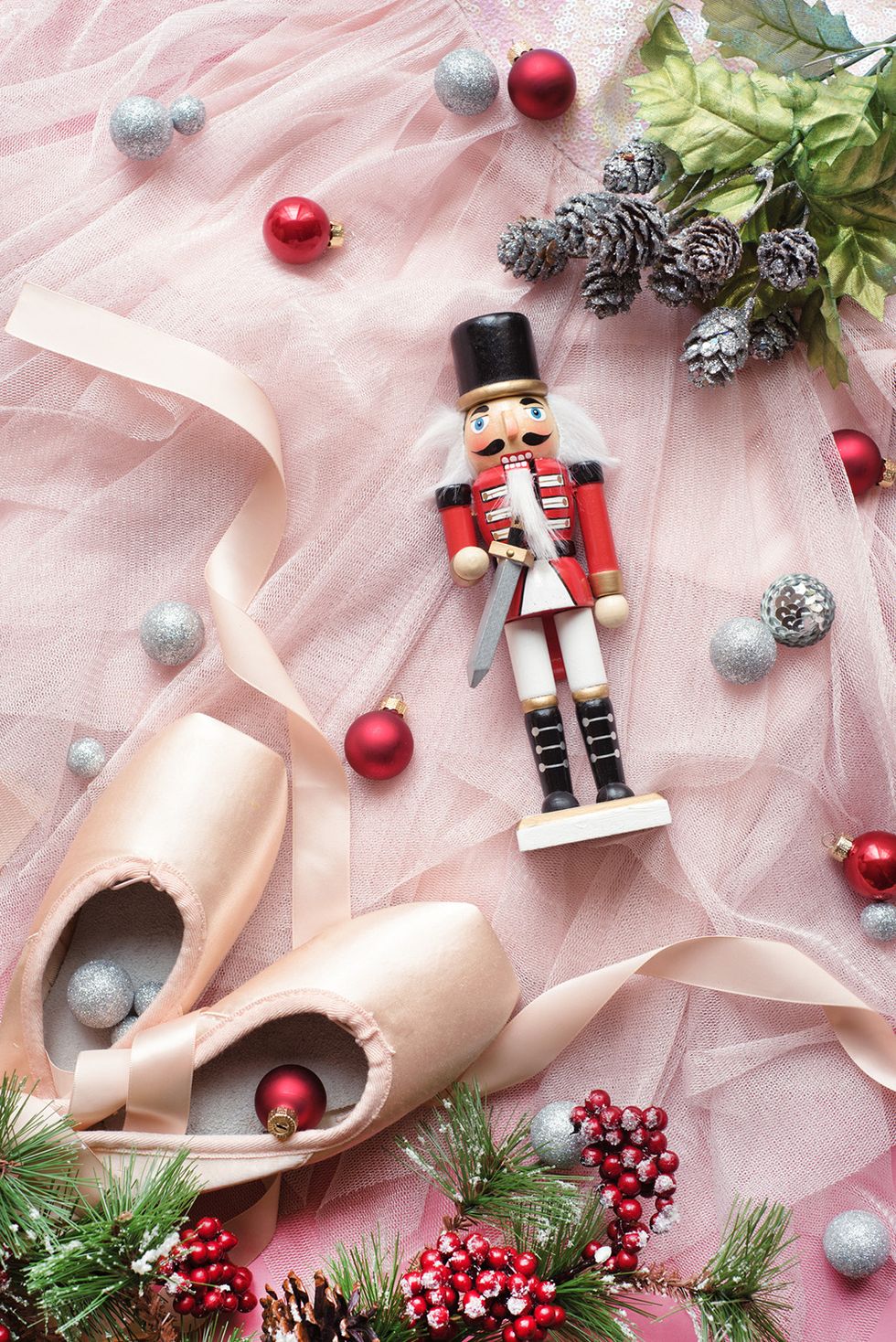 a wooden nutcracker laid next to pink ballet shoes
