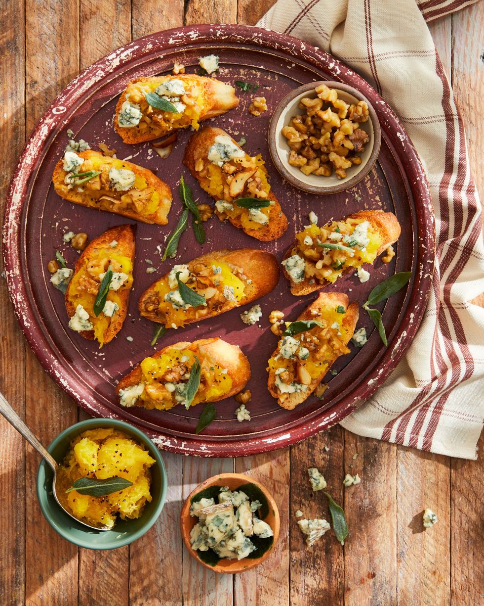 smashed acorn squash and garlicky walnut crostini arranged on a dark maroon serving plate with crumbled blue cheese and fried sage