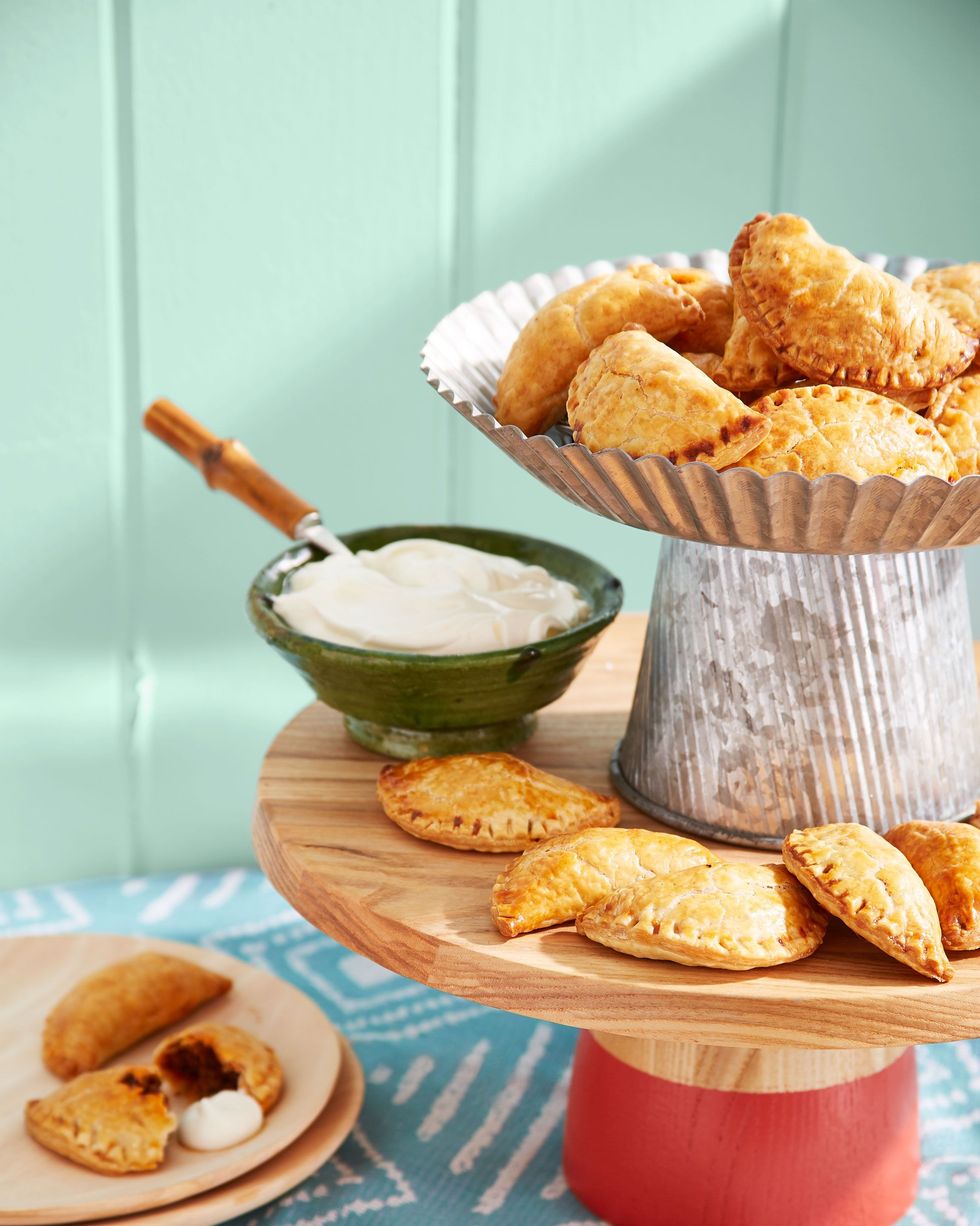 beef and raisin empanadas on serving stands with a small bowl of sour cream
