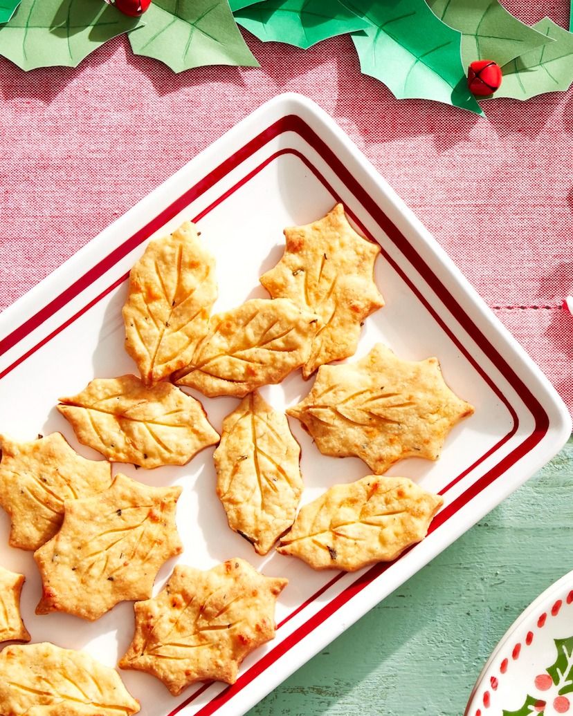 cheddar crackers cut into the shape of holly leaves arranged on a rectangle serving plate