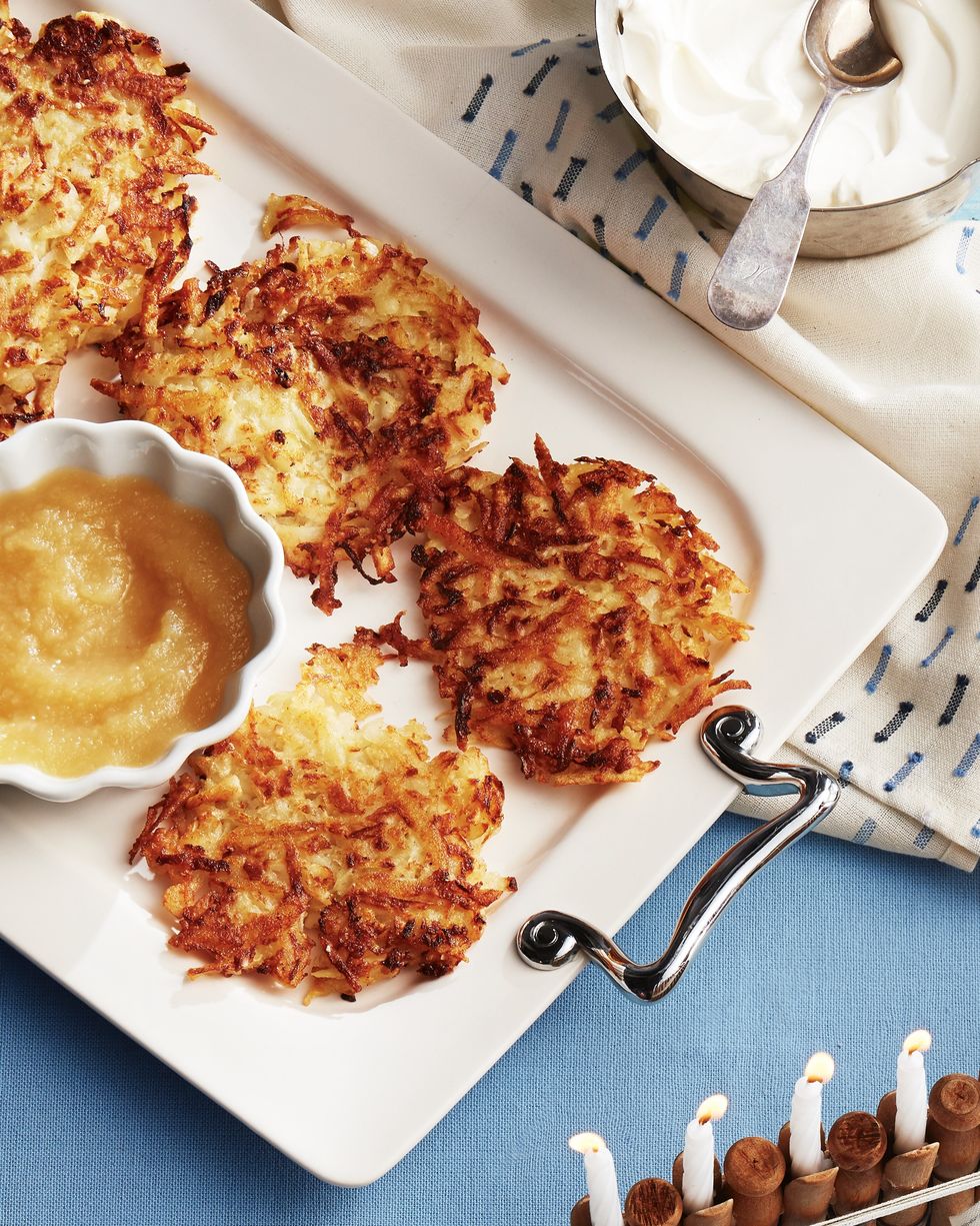 potato and parsnip latkes arranged on a white serving tray with a small bowl of applesauce and a small bowl of sour cream for serving