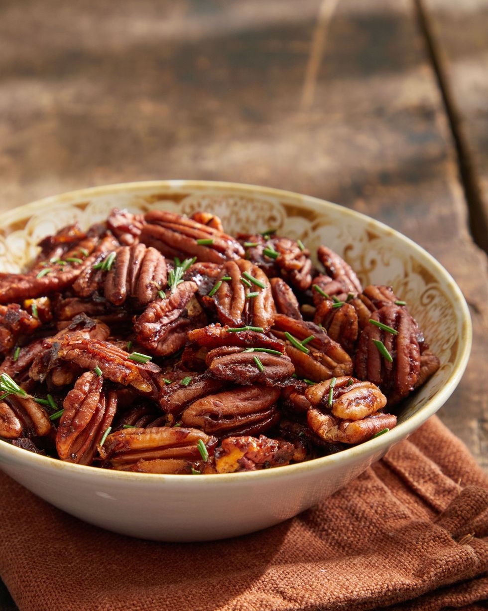 sweet and spicy roasted pecans garnished with chopped rosemary, in a bowl on a light brown kitchen towel