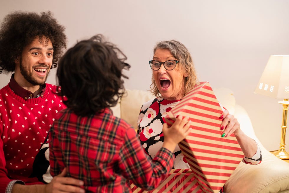 older woman sitting next to man on couch receiving a christmas gift from a young boy