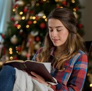 christmas bible verses  woman with eyes closed reading a bible in front of a christmas tree