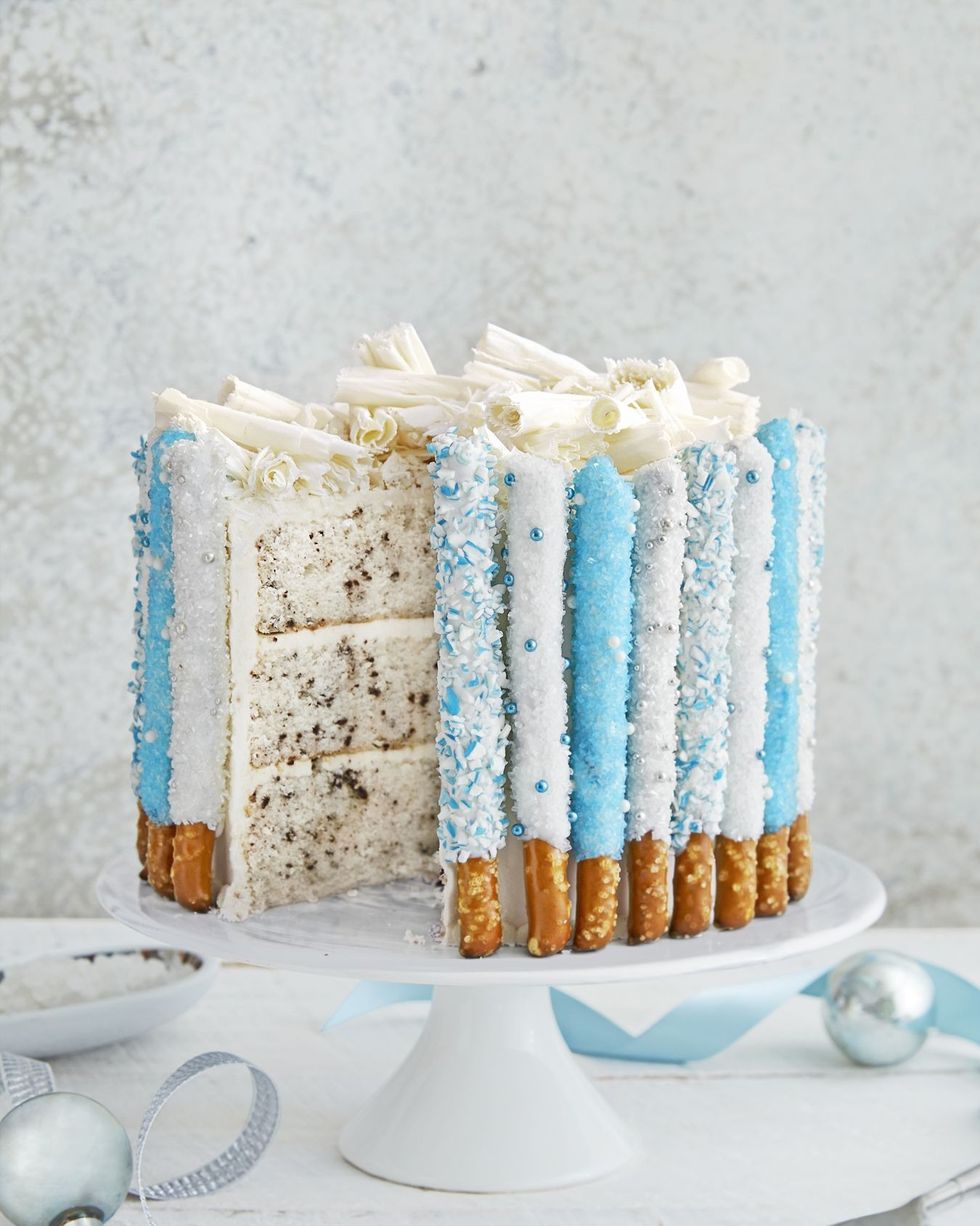 three layer chocolate chip cake with candied pretzel rods lining the outside of the cake with white chocolate curls on top